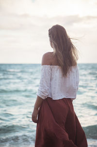 Rear view of woman standing at beach against sky
