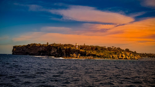 Sea by buildings against sky during sunset