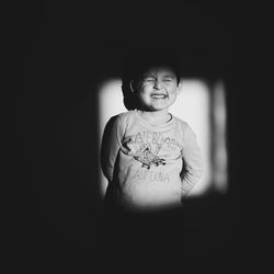 Portrait of smiling girl standing against black background