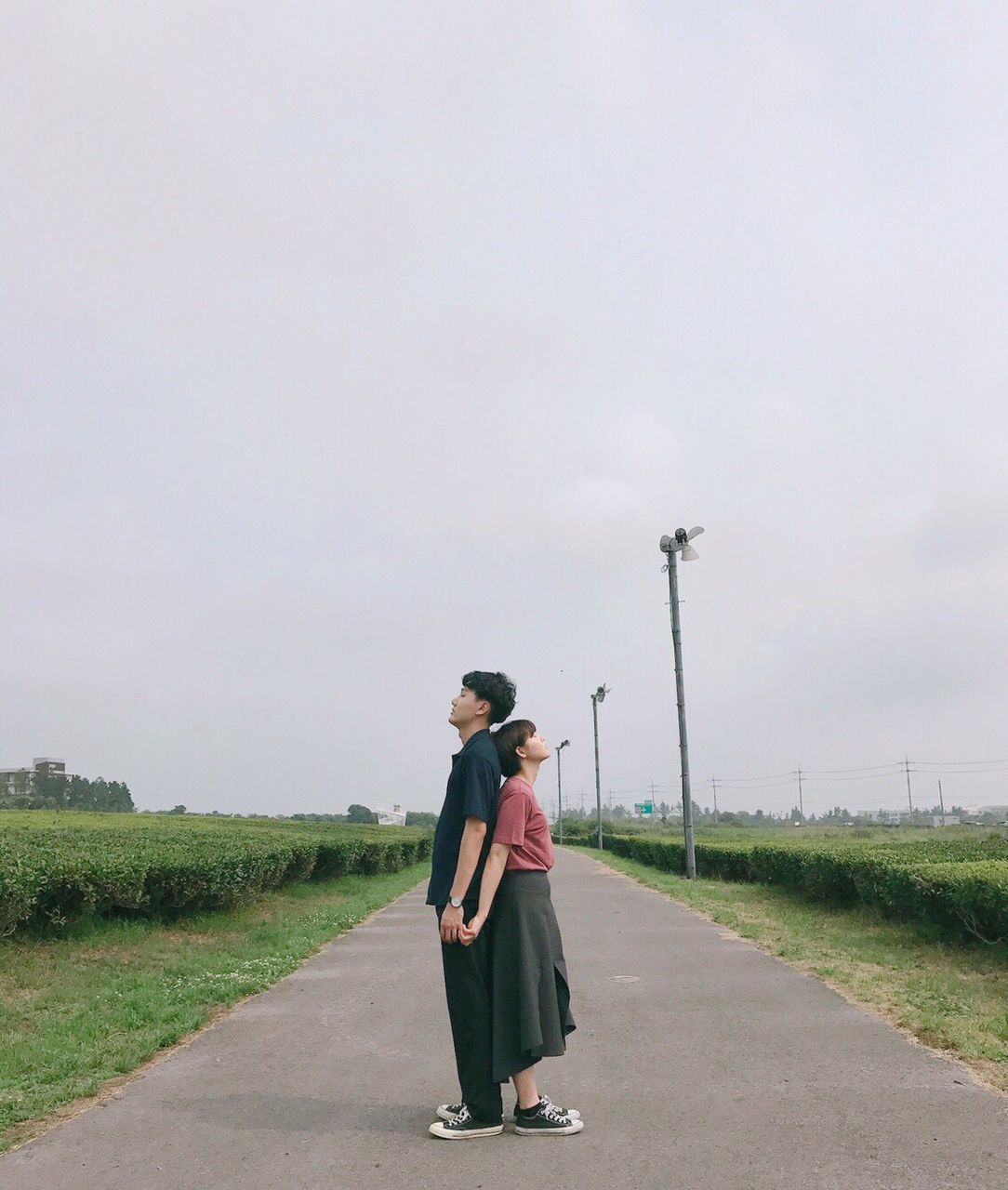 YOUNG COUPLE STANDING ON ROAD AGAINST CLEAR SKY