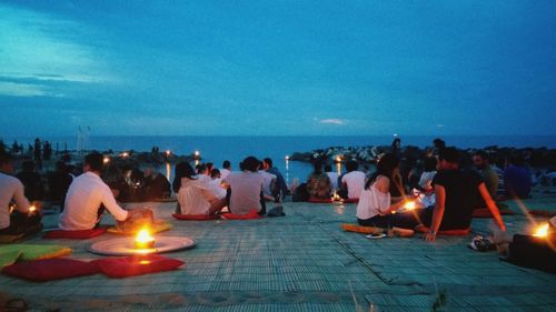 People sitting on shore by sea against sky