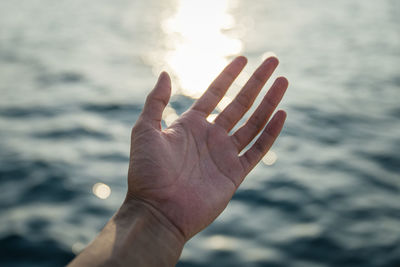 Cropped image of hand against sea against sky