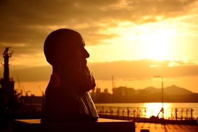 Side view of a statue against river at sunset