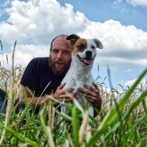 Portrait of smiling man with dog by plants on field