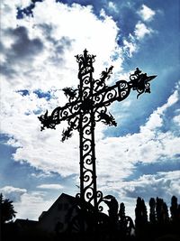 Low angle view of weather vane against cloudy sky