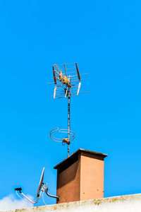 Low angle view of communications tower against building against clear blue sky