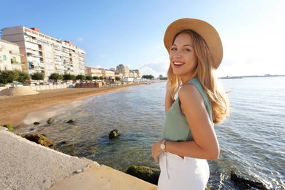 Happy stylish woman turns around and smiling at camera on crotone seafront in calabria, italy