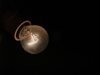 Low angle view of illuminated light bulb against black background