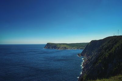 Scenic view of sea and cliff against clear blue sky