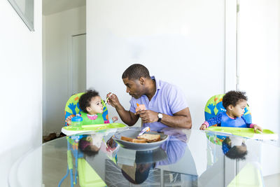 Father feeding baby girl while sitting by daughter at table