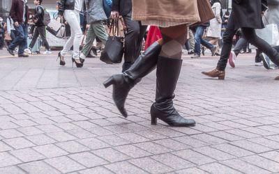 Low section of woman wearing high heels boots walking on paved street