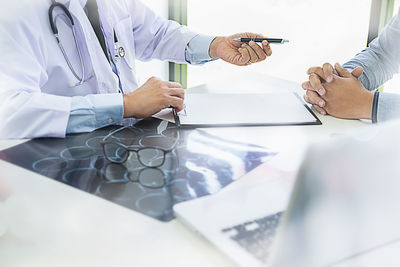Midsection of doctor giving pen to patient at table