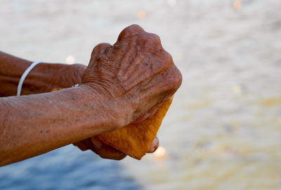 Close-up of hand holding stone against sea