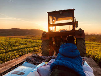 Man lying on mattress by tractor against sky during sunset