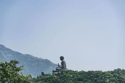 Rear view of man sitting on rock against sky