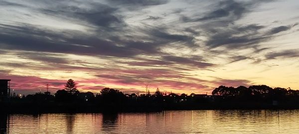 Silhouette trees by lake against sky during sunset