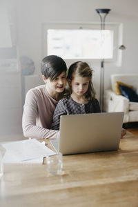 Mother and daughter watching laptop together at desk