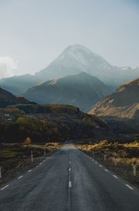 Empty road leading towards mountains against sky