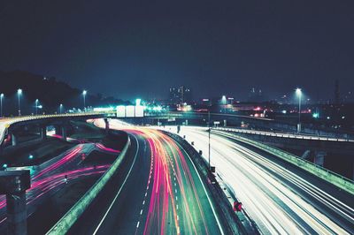 Illuminated light trails on highway in city against sky at night