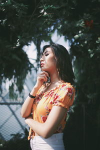 Young woman looking away while standing against tree