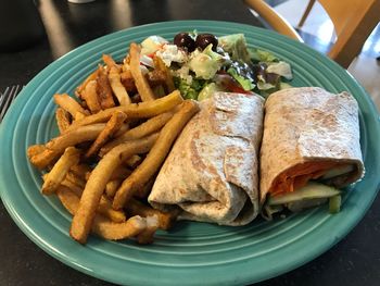 Close-up of spare rib wrap with french fries and greek salad served on table