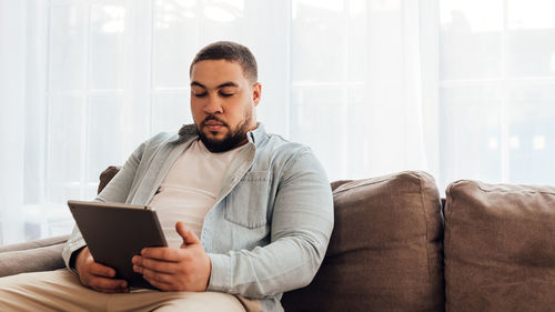 Man using digital tablet while sitting on sofa at home