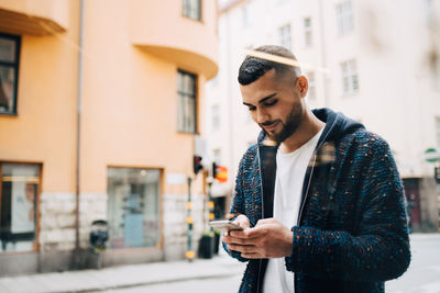 Confident young businessman text messaging on smart phone seen through window