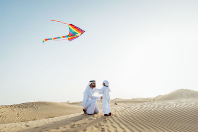 Man and woman standing on sand against clear sky