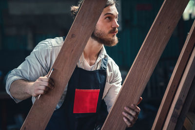 Young man looking away while sitting on wood