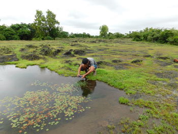 Full length of boy photographing by pond on field