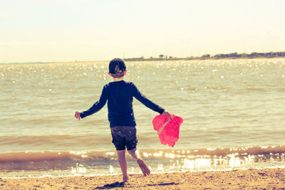 Rear view of boy standing on beach against sky