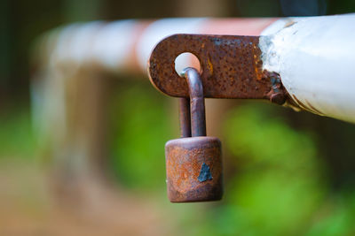 Close-up of rusty padlock hanging on barricade on field