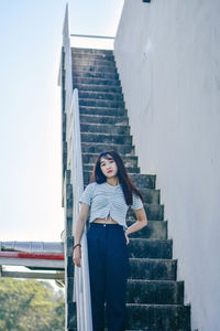 Portrait of young woman standing on staircase by railing at building terrace