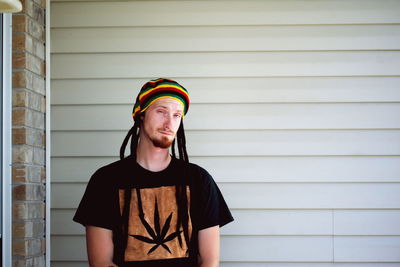 Portrait of young man with dreadlocks against wall