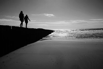 Silhouette men on beach against sky