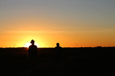 Silhouette people standing on field against sky during sunset