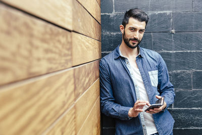 Young man using mobile phone while standing on wall