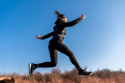 Young female runner is jumping over wooden hurdles in countryside - concept of health and wellness
