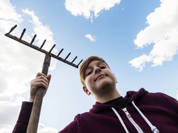 Low angle portrait of smiling boy holding camera against sky