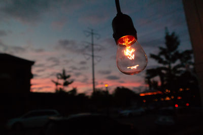 Low angle view of illuminated light bulb against sky at sunset