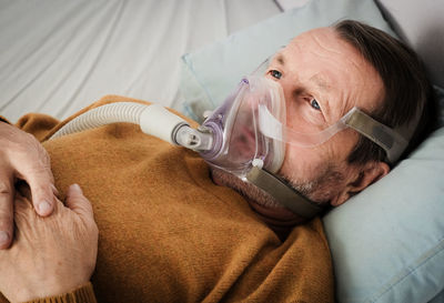 Senior man wearing oxygen mask lying on hospital bed