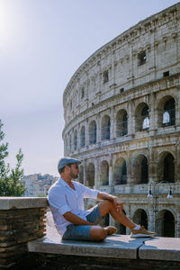 Man sitting by historical building against sky