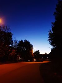 Silhouette trees by road against clear blue sky at night