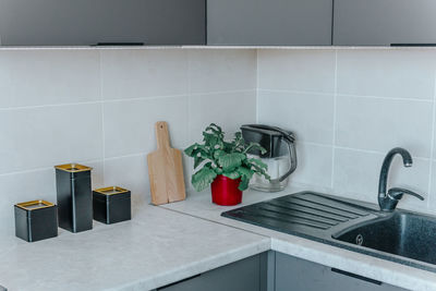 On the kitchen countertop are a chopping board, black containers, a flower in a red board