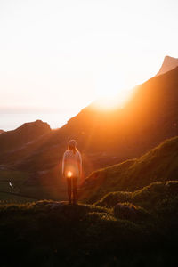 Rear view of man standing on mountain against sky during sunset