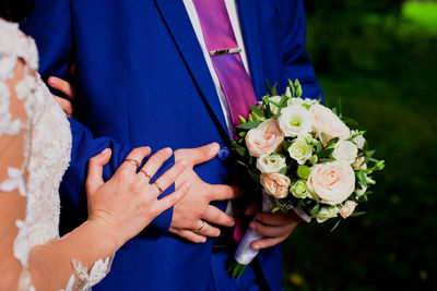 Midsection of bride and groom holding bouquet during wedding ceremony