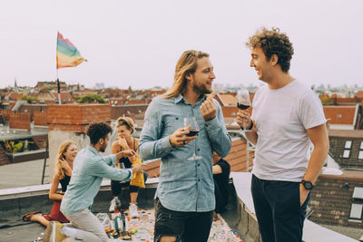 Friends having wine and talking while friends enjoying on terrace at rooftop party