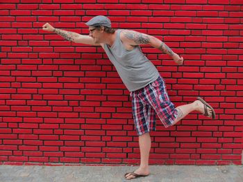 Hipster imitating superhero while standing on sidewalk against red wall