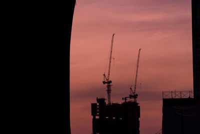 Silhouette cranes against sky at sunset