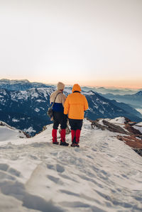 Rear view of man walking on snowcapped mountain against sky